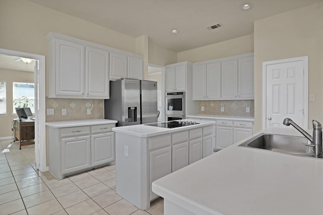 kitchen with sink, appliances with stainless steel finishes, white cabinets, a kitchen island, and light tile patterned flooring