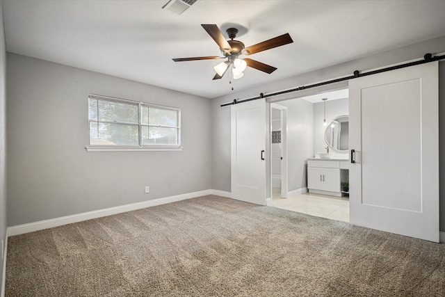 unfurnished bedroom featuring a barn door, light colored carpet, connected bathroom, and ceiling fan