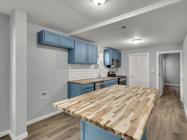 kitchen featuring butcher block countertops, blue cabinetry, backsplash, stainless steel appliances, and light wood-type flooring