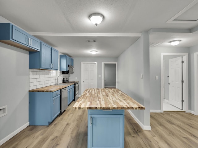 kitchen with blue cabinets, sink, butcher block countertops, appliances with stainless steel finishes, and decorative backsplash