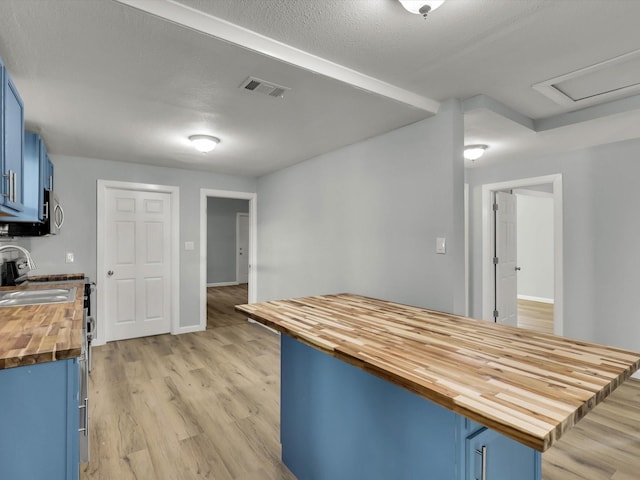 kitchen with a breakfast bar, blue cabinets, butcher block counters, sink, and light hardwood / wood-style flooring