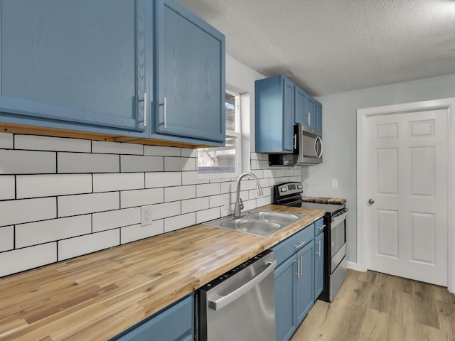 kitchen featuring wood counters, blue cabinets, sink, stainless steel appliances, and backsplash