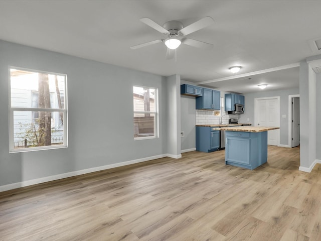 kitchen featuring blue cabinets, butcher block counters, tasteful backsplash, light wood-type flooring, and stainless steel appliances