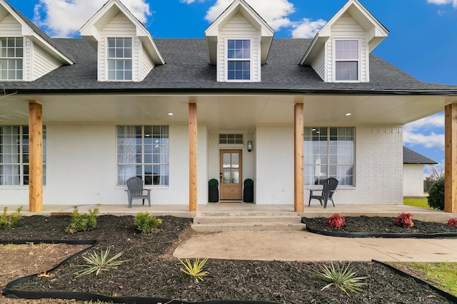 new england style home featuring a porch, brick siding, and a shingled roof