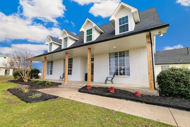 cape cod home featuring covered porch, brick siding, and a front lawn