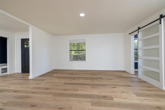 unfurnished room with a barn door, baseboards, and light wood-style flooring