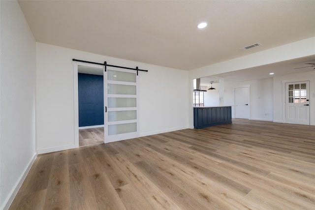 empty room with a barn door, wood finished floors, visible vents, and baseboards