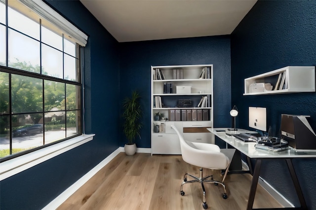 office featuring a textured wall, built in desk, baseboards, and wood finished floors