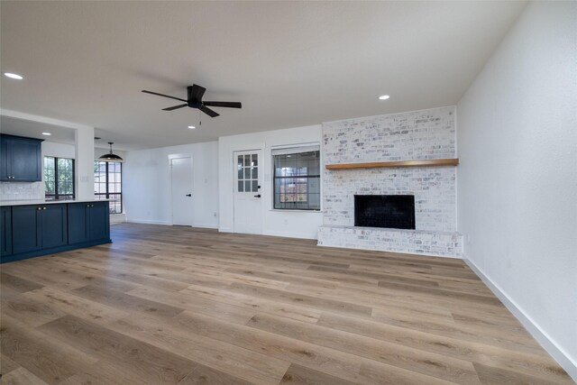 unfurnished living room with ceiling fan, a brick fireplace, and light hardwood / wood-style floors