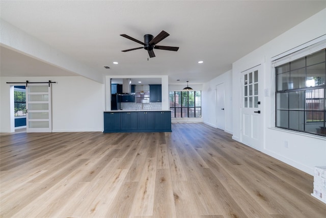 unfurnished living room featuring ceiling fan, a barn door, light wood-style flooring, visible vents, and baseboards