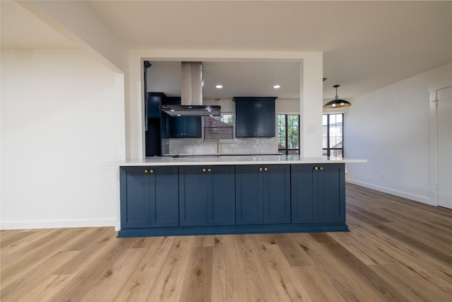 kitchen with blue cabinetry, decorative light fixtures, light hardwood / wood-style flooring, island exhaust hood, and decorative backsplash