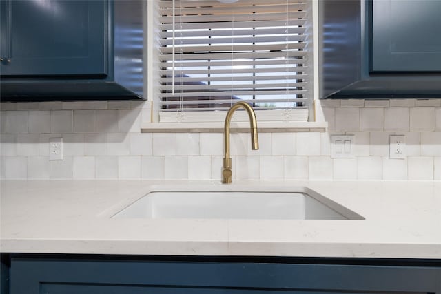 room details with blue cabinets, light stone countertops, backsplash, and a sink