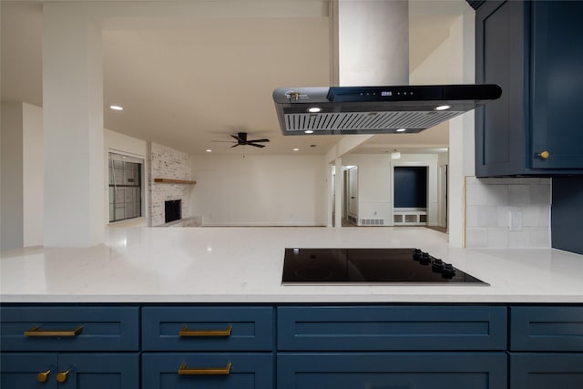 kitchen featuring blue cabinetry, ceiling fan, a large fireplace, black electric cooktop, and exhaust hood