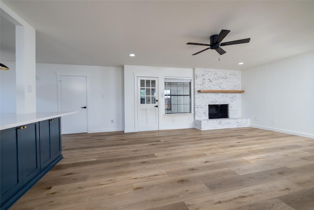 unfurnished living room featuring recessed lighting, light wood-style floors, a ceiling fan, a brick fireplace, and baseboards