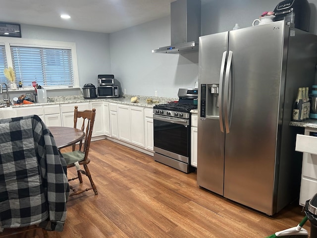 kitchen with white cabinetry, light stone counters, light hardwood / wood-style floors, stainless steel appliances, and wall chimney range hood