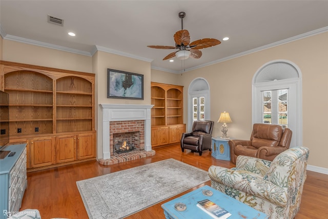 living room featuring light hardwood / wood-style flooring, a fireplace, ornamental molding, and ceiling fan