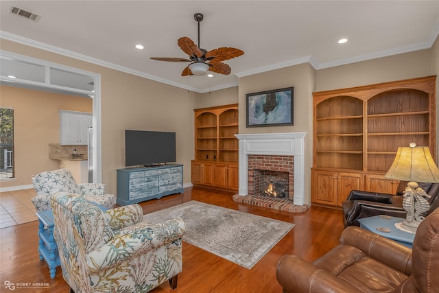 living room featuring a fireplace, crown molding, wood-type flooring, and ceiling fan