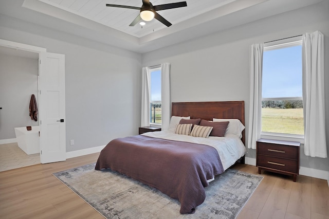 bedroom with a raised ceiling, light wood finished floors, baseboards, and a ceiling fan