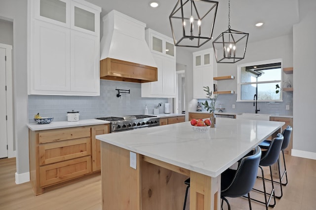 kitchen with premium range hood, sink, a kitchen island, white cabinets, and stove