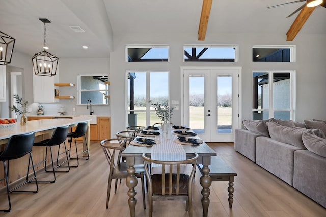 dining space with beam ceiling, french doors, light wood-style flooring, and ceiling fan with notable chandelier