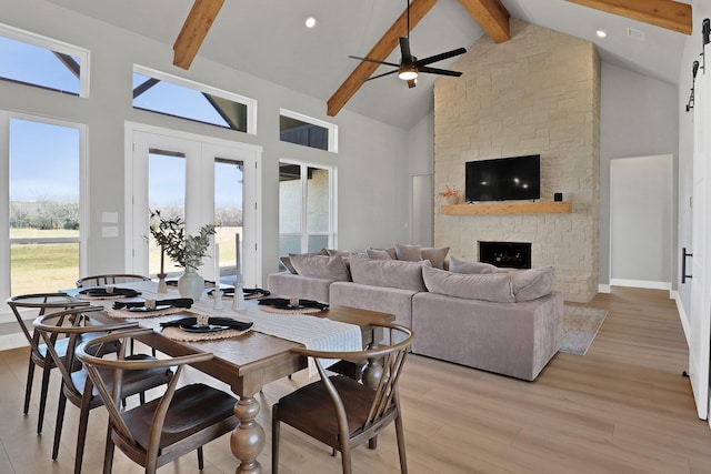 dining room with beamed ceiling, high vaulted ceiling, light wood-type flooring, and a fireplace