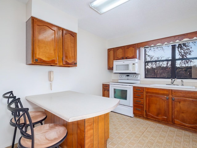 kitchen featuring sink, white appliances, a breakfast bar area, vaulted ceiling, and kitchen peninsula