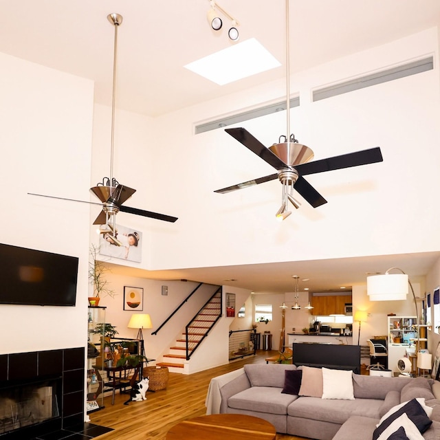 living area featuring stairs, a tiled fireplace, wood finished floors, and a ceiling fan