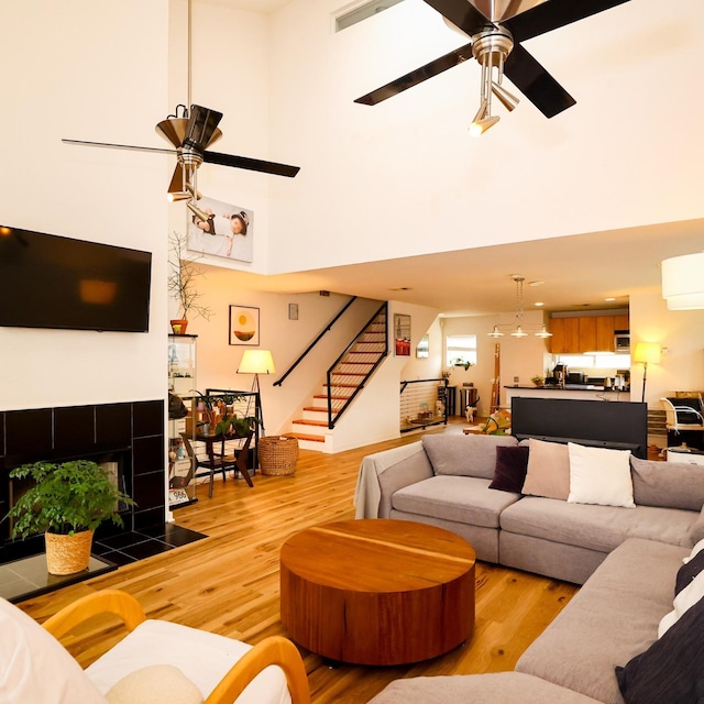 living room with stairs, light wood-type flooring, a fireplace, and a ceiling fan