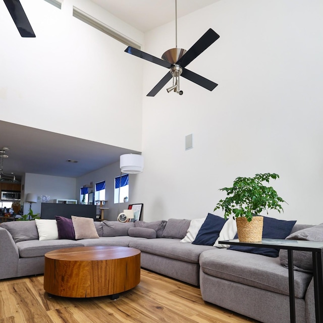 living room featuring a towering ceiling, ceiling fan, and light hardwood / wood-style flooring