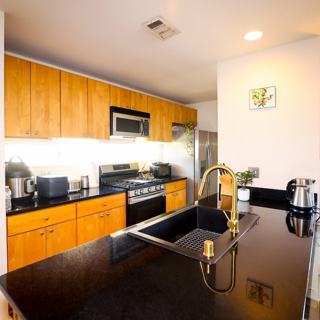 kitchen featuring visible vents, brown cabinetry, dark countertops, appliances with stainless steel finishes, and a sink