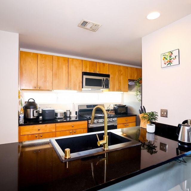 kitchen with stainless steel appliances, brown cabinetry, dark countertops, and visible vents