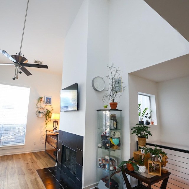 living room featuring ceiling fan, a towering ceiling, a fireplace, and light hardwood / wood-style flooring