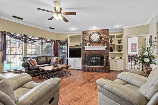 living room with hardwood / wood-style floors, built in features, ornamental molding, ceiling fan, and a brick fireplace