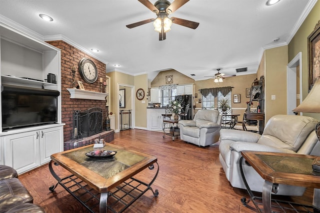 living room with wood-type flooring, crown molding, ceiling fan, and a fireplace