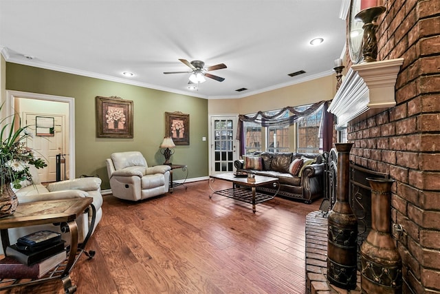 living room with a brick fireplace, wood-type flooring, ornamental molding, and ceiling fan