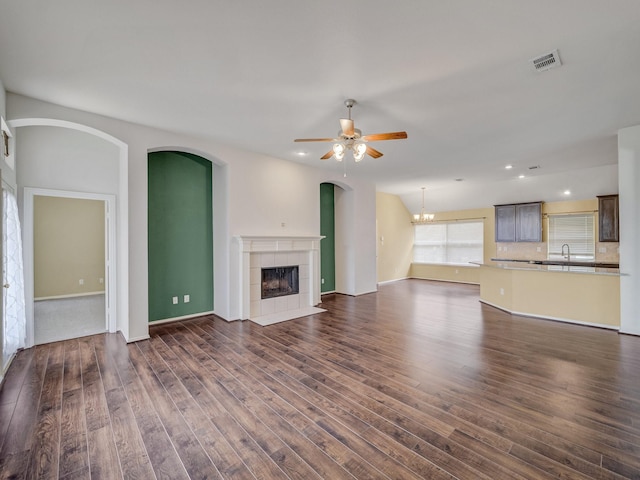 unfurnished living room with sink, dark wood-type flooring, a fireplace, and ceiling fan with notable chandelier