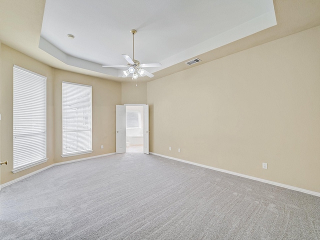 empty room featuring a raised ceiling, light colored carpet, and ceiling fan