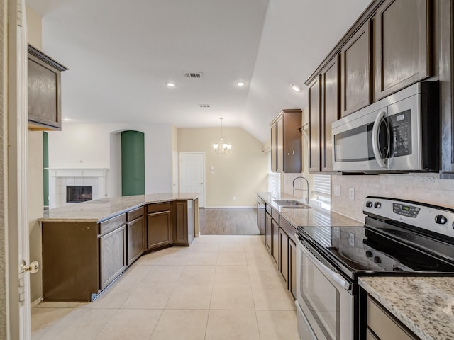 kitchen with decorative light fixtures, lofted ceiling, sink, light stone counters, and stainless steel appliances