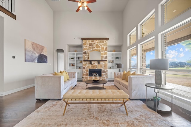 living room with built in features, a fireplace, a high ceiling, ceiling fan, and dark wood-type flooring