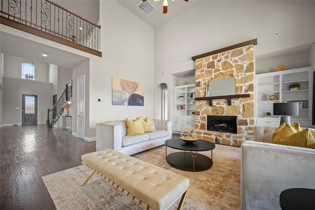 living room featuring dark hardwood / wood-style flooring, a stone fireplace, ceiling fan, and a towering ceiling