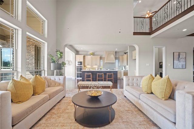 living room with ceiling fan, a towering ceiling, and light hardwood / wood-style floors