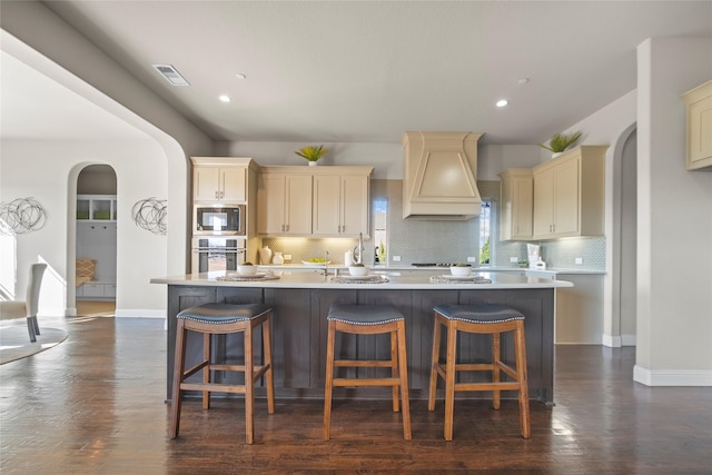 kitchen featuring a kitchen island with sink, a kitchen breakfast bar, custom range hood, and appliances with stainless steel finishes