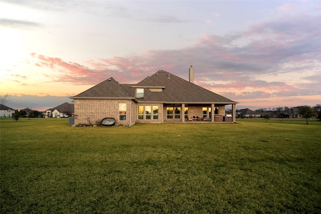 back house at dusk featuring a patio and a lawn