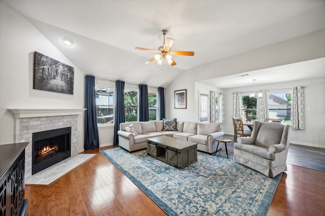 living room with lofted ceiling, a brick fireplace, ceiling fan with notable chandelier, and dark wood-type flooring