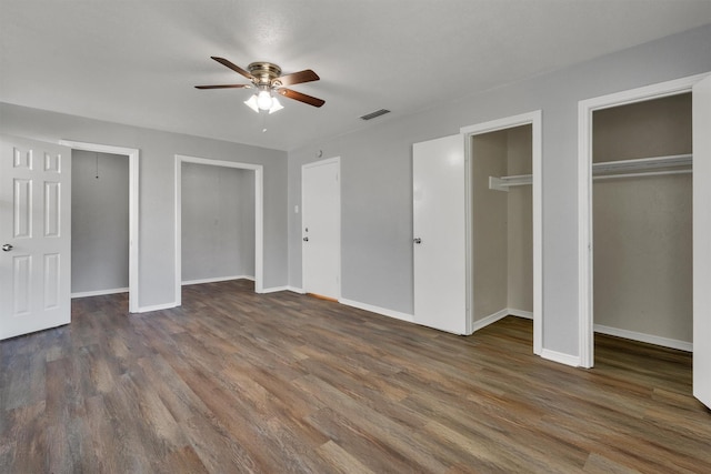 unfurnished bedroom with ceiling fan, dark hardwood / wood-style floors, and two closets