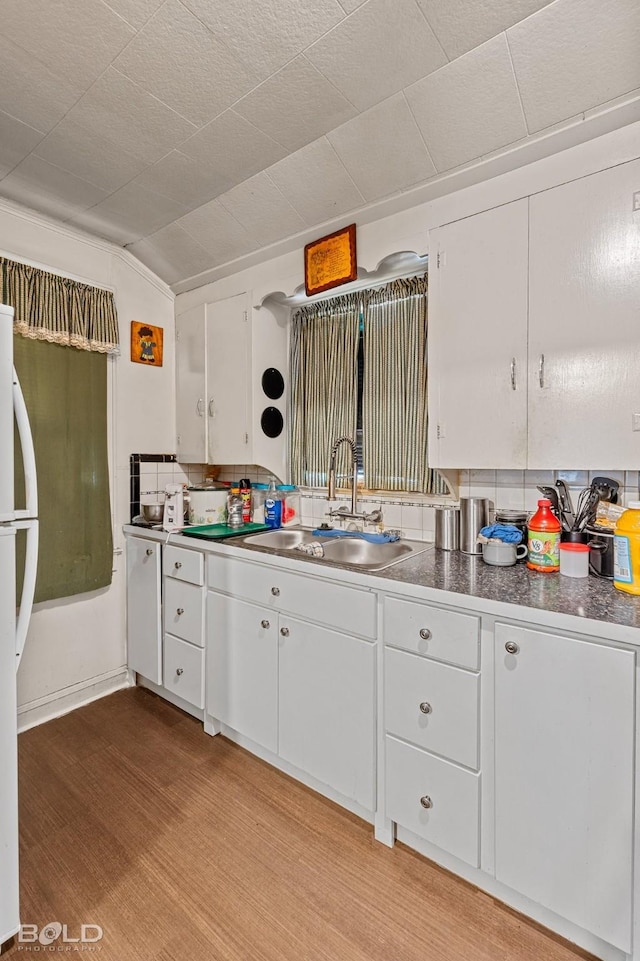 kitchen with vaulted ceiling, white cabinetry, sink, white refrigerator, and light hardwood / wood-style floors