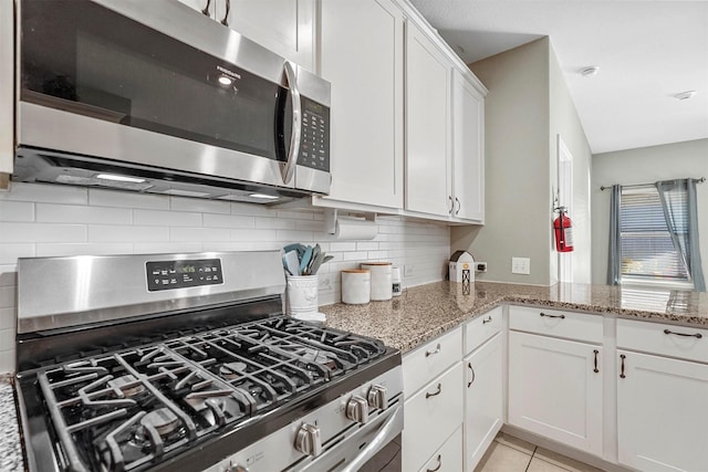 kitchen with light tile patterned flooring, white cabinets, appliances with stainless steel finishes, backsplash, and light stone countertops