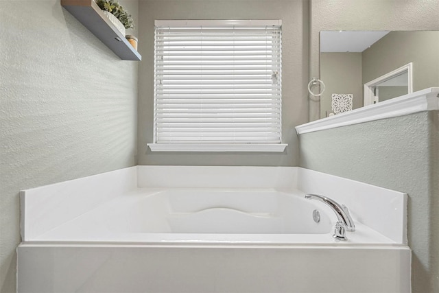 bathroom featuring a healthy amount of sunlight, a bath, and a textured wall