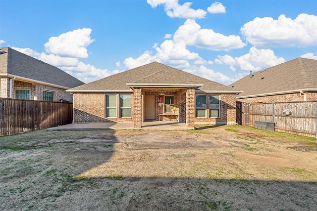 rear view of house featuring a patio, brick siding, roof with shingles, and a fenced backyard