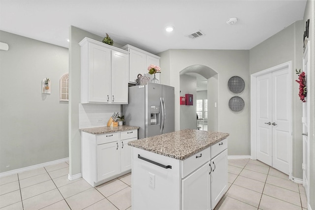 kitchen featuring arched walkways, light tile patterned floors, visible vents, white cabinets, and stainless steel fridge